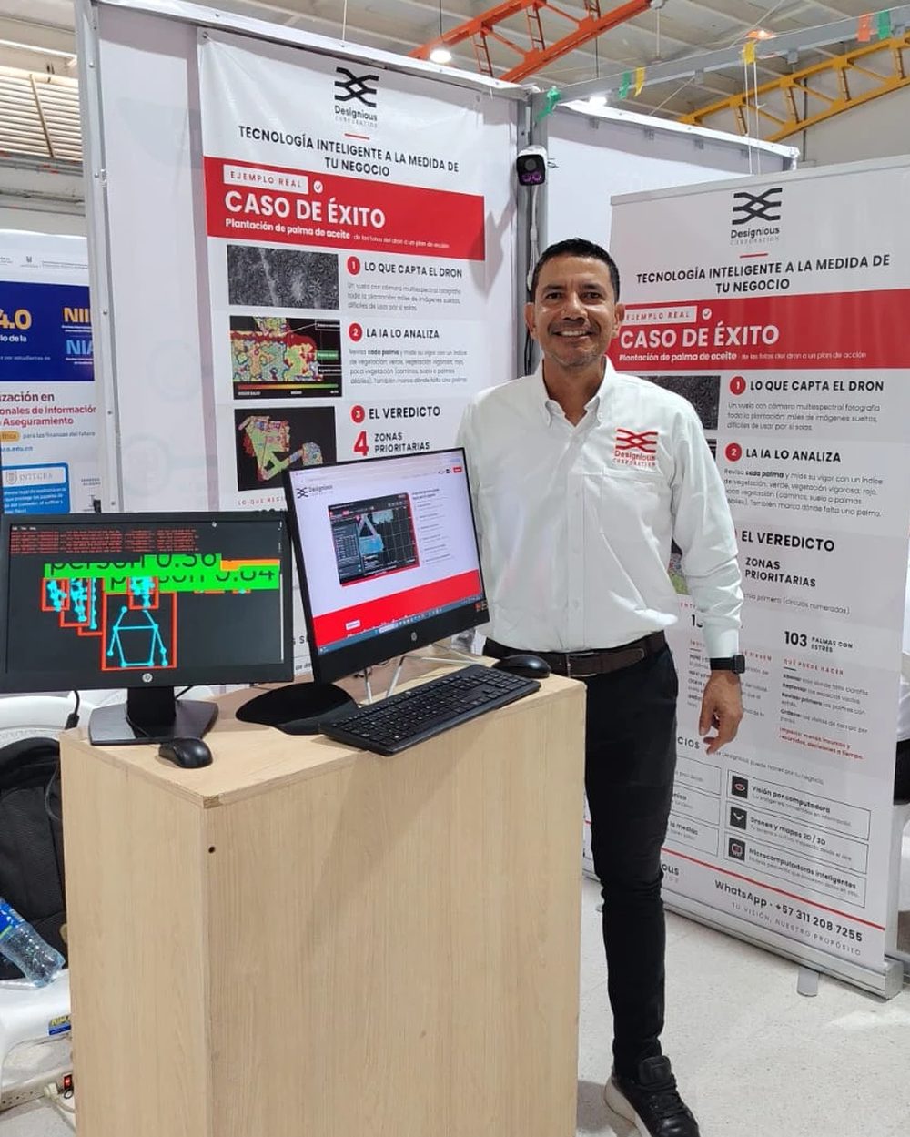 Stand de Designious Corporation con dos pantallas: análisis de comportamiento humano con cámara infrarroja y el caso de éxito de la palma, junto al cartel del caso